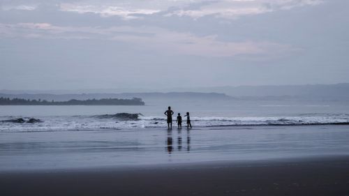Men standing on beach against sky