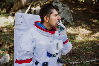 Man in spacesuit smoking cigarette while standing on land in forest