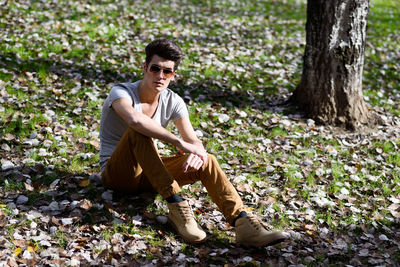 Young man wearing sunglasses sitting on field in forest