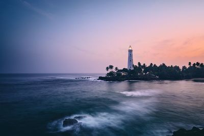 Lighthouse in sea against sky during sunset