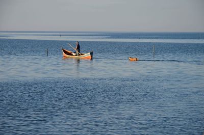 Man standing on rowboat in sea against sky