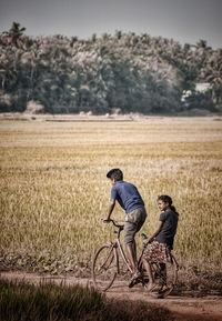 Man riding bicycle with sister on dirt road by farm