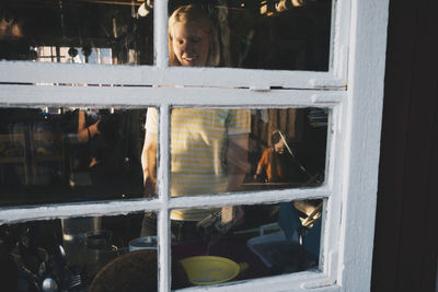 Smiling woman cooking food seen from glass window