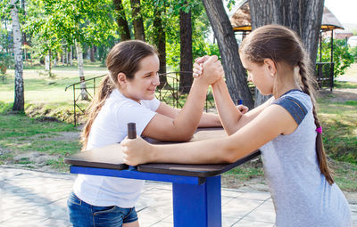 Girls arm wrestling on table in park