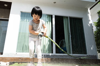 Full length of cute girl holding garden hose outdoors