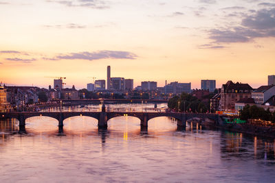 Bridge over river by buildings against sky during sunset