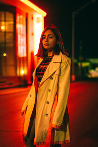 Portrait of woman standing by illuminated street at night