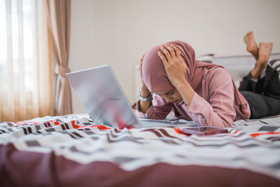 Woman using digital tablet while sitting on bed at home