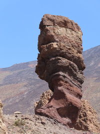 Rock formation by mountain against clear sky