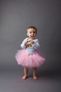 Baby girl wearing dress standing against gray background