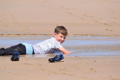 Portrait of smiling boy lying on shore at beach