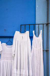 White dresses hanging on gate against blue wall at market