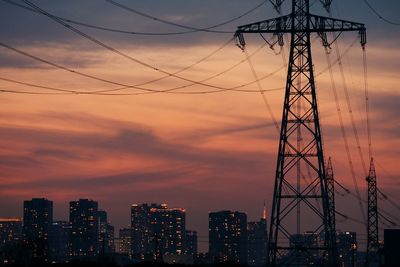 Low angle view of electrical tower in city against cloudy sky