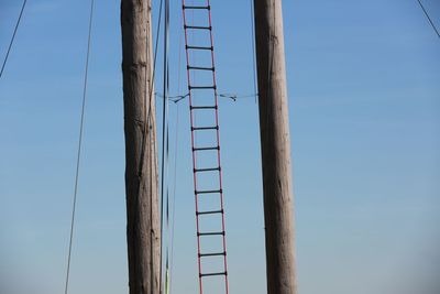 Low angle view of wooden poles and ladder against clear blue sky