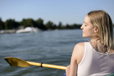 Young woman with eyes closed holding oar while sitting in rowboat