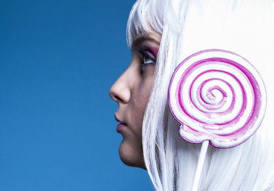 Side view close-up of woman with lollipop against blue background