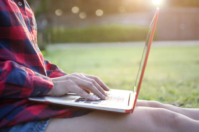 Midsection of woman using laptop while sitting on field at park