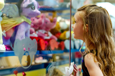 Girl looking at stuffed toy in store through glass window