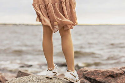 A young woman stands on the rocky shore of the sea. a dress flying in the wind close-up.