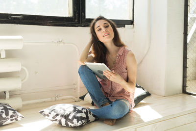 Young woman using phone while sitting on floor