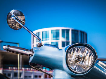 Close-up of motorcycle handle and building against clear blue sky