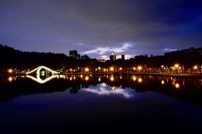 Illuminated buildings by lake against sky at night