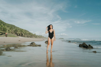 Latina woman wearing black swimwear touching her hair on a beautiful beach