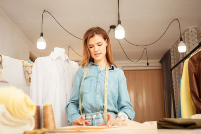 Portrait of seamstress woman in atelier. beautiful room, dummy with white shirt, counter with ready 