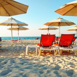 Deck chairs and parasols on beach against sky