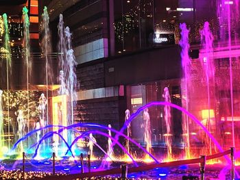 Illuminated ferris wheel against buildings at night