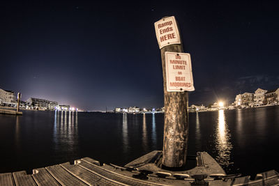 Information sign by river in city at night