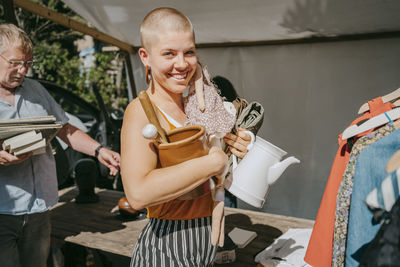 Side view portrait of happy female customer holding various objects while shopping at flea market