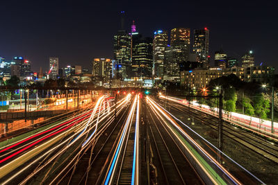 High angle view of train light trails amidst buildings in city at night