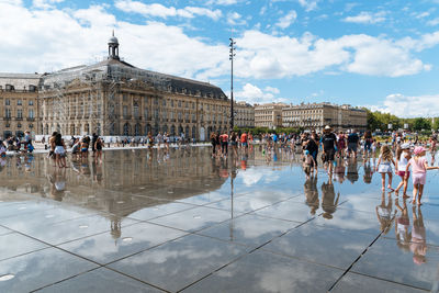 People on wet street against cloudy sky in city