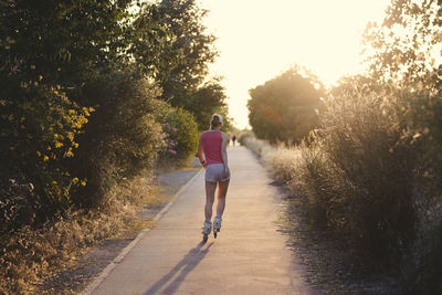 Rear view of woman inline skating on road amidst plants