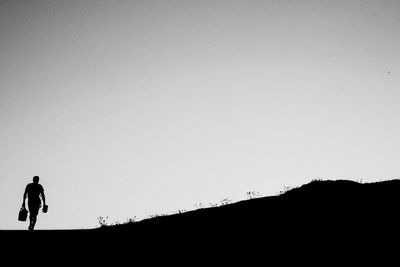 Silhouette man walking on landscape against clear sky