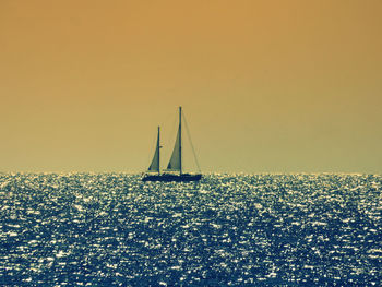 Silhouette sailboat sailing on sea against sky during sunset