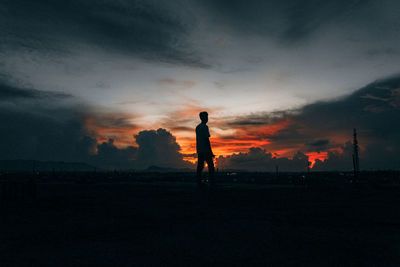 Silhouette man standing on field against sky during sunset