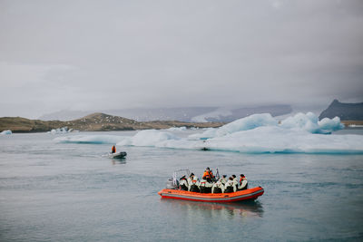 People in boat sailing on sea against sky