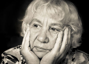 Sad senior woman against black background