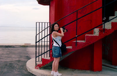 Full length of woman standing by red lifeguard hut at beach