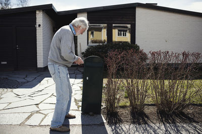 Full length of senior man standing by mailbox outside house during sunny day