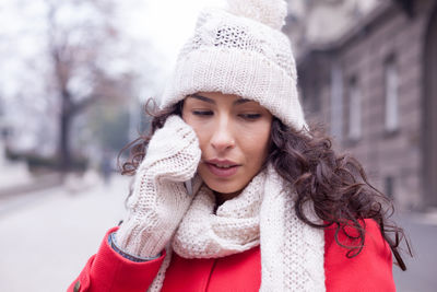 Young woman in warm clothing talking on smart phone while standing on city street