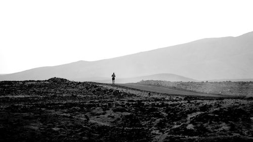 Person on road by field against clear sky