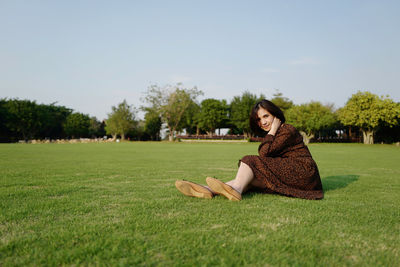 Portrait of woman sitting on field against sky