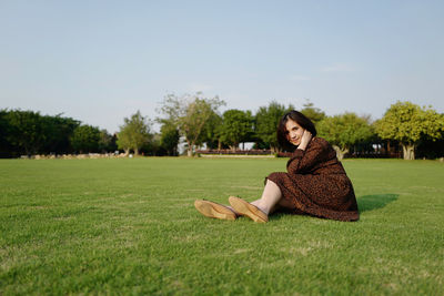 Woman sitting on field against sky