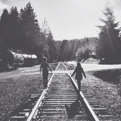 Rear view of people walking on railroad track against sky