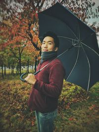 Portrait of man with umbrella standing in forest during autumn