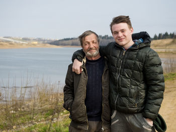 Portrait of smiling son and father standing against lake