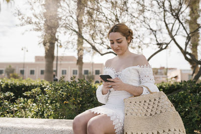 Young woman using phone while sitting on tree